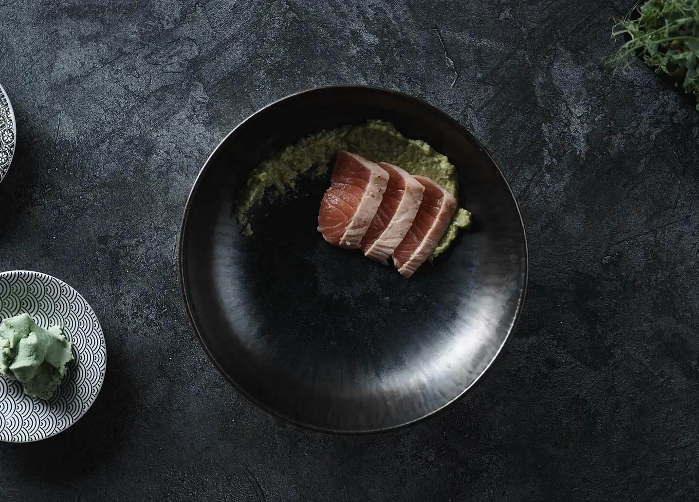 Sliced tuna sashimi with green puree on dark plate