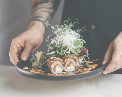 Chef holding sushi rolls with salad garnish on plate