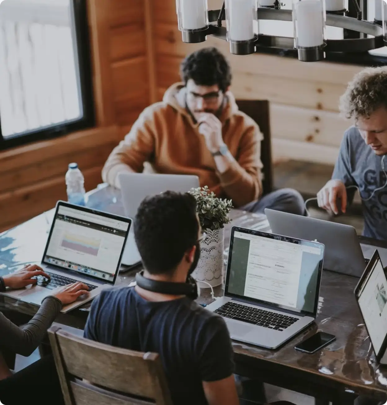 Group of people collaborating with laptops at a coworking table in wooden workspace.