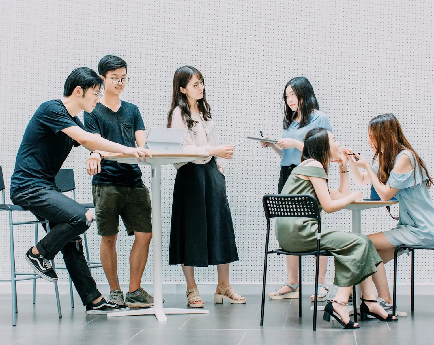 A group of six young adults in casual clothing interacting in a modern, minimalist setting